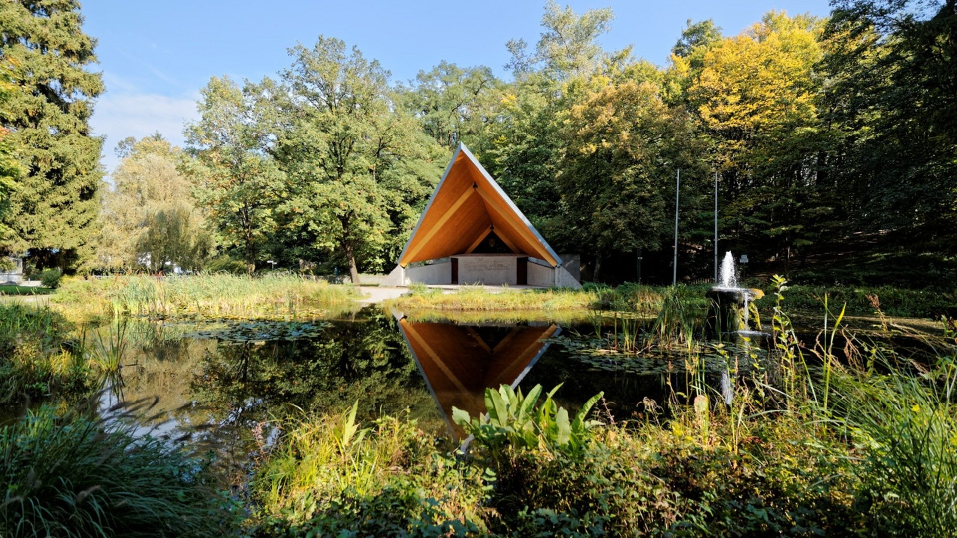 Triangle wooden roof structure with pond and forest in the foreground