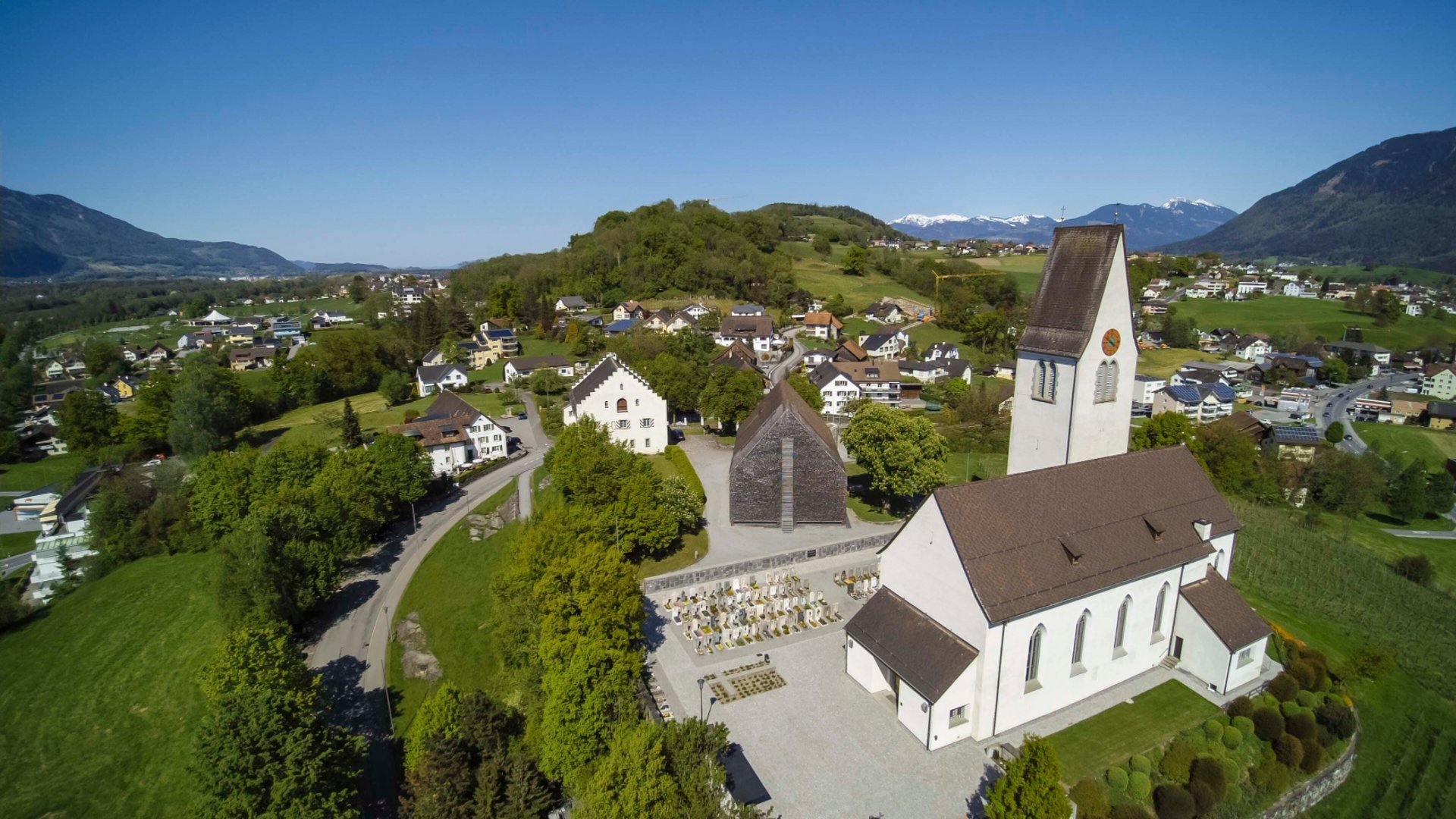 Aerial view of a village with a church and mountains in the background