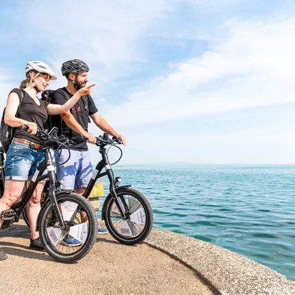 Twee fietsers met helmen kijken naar het water en wijzen vooruit