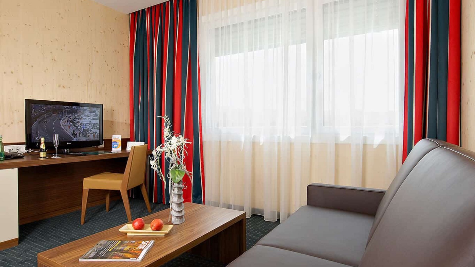 Hotel room with brown sofa, wooden table, desk, and TV