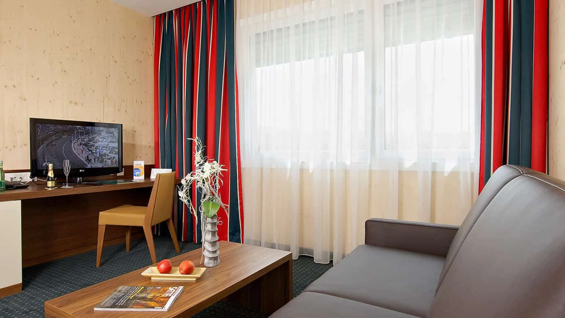 Hotelkamer met bruine bank, houten tafel, bureau en tv