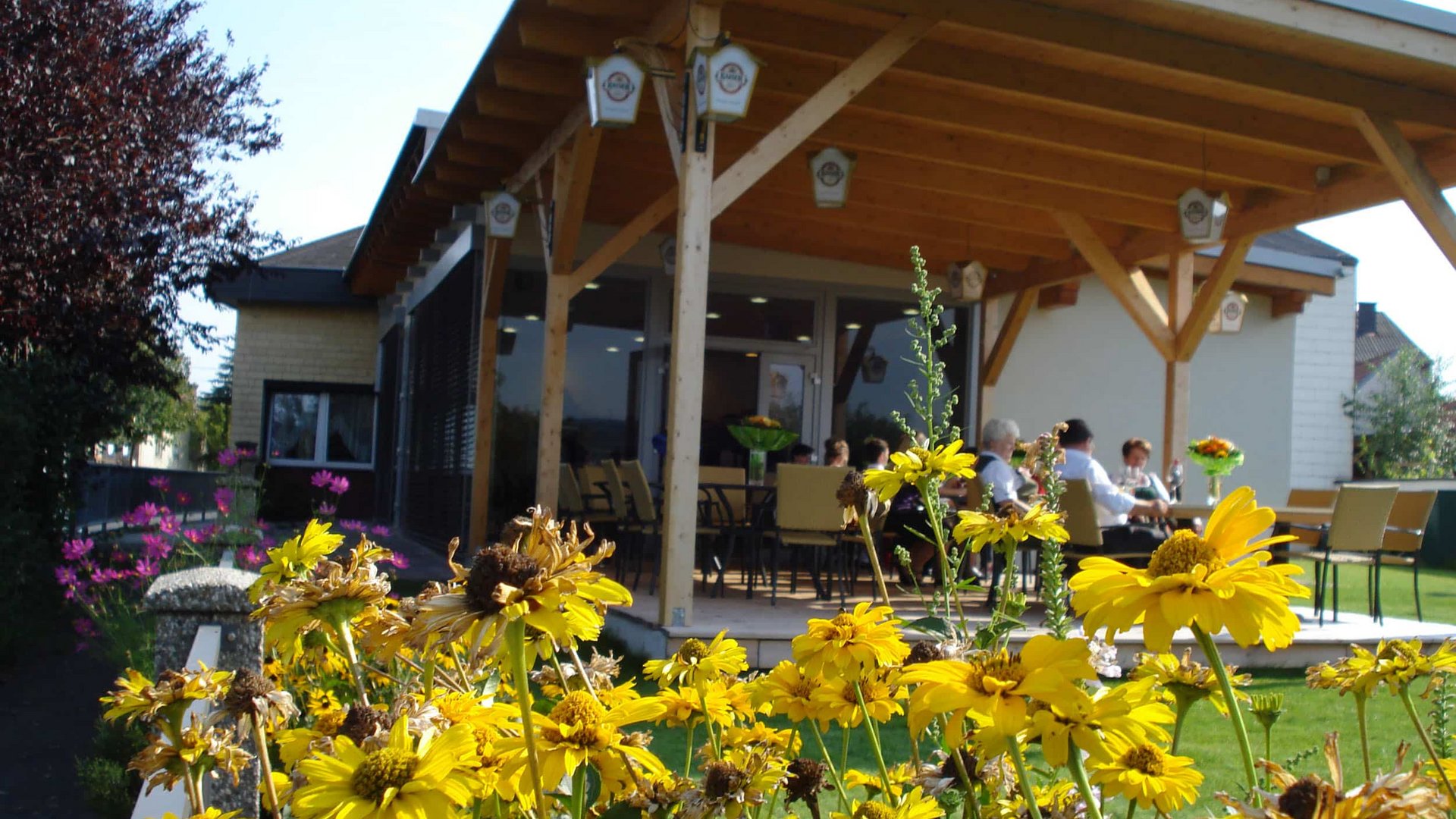 Yellow flowers in front of a patio with people sitting on chairs