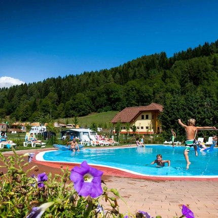 Children jumping into a pool at a campsite surrounded by mountains