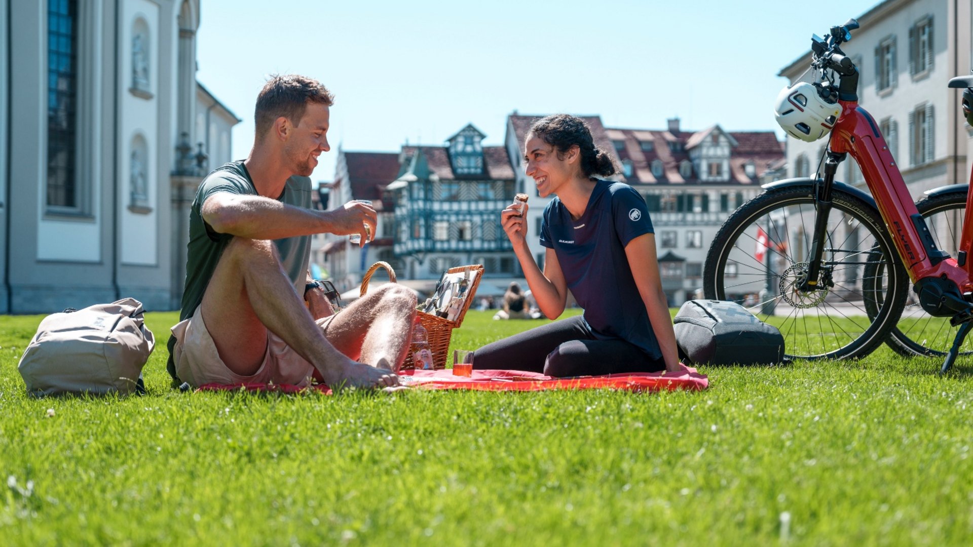 Couple picnic on grass with bike and basket on a sunny day in town