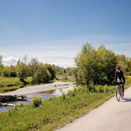 Fahrradfahrerin auf einem Weg neben einem Fluss in grüner Landschaft