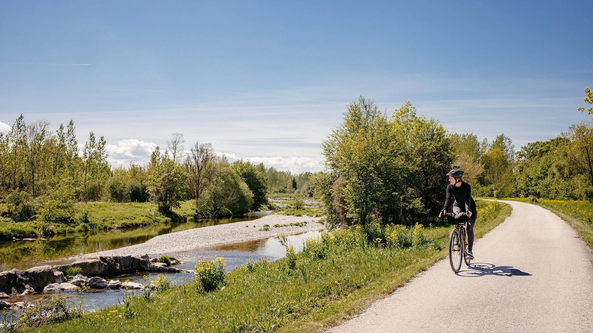 Traisental-Radweg Fahrradfahrerin auf einem Weg neben einem Fluss in grüner Landschaft