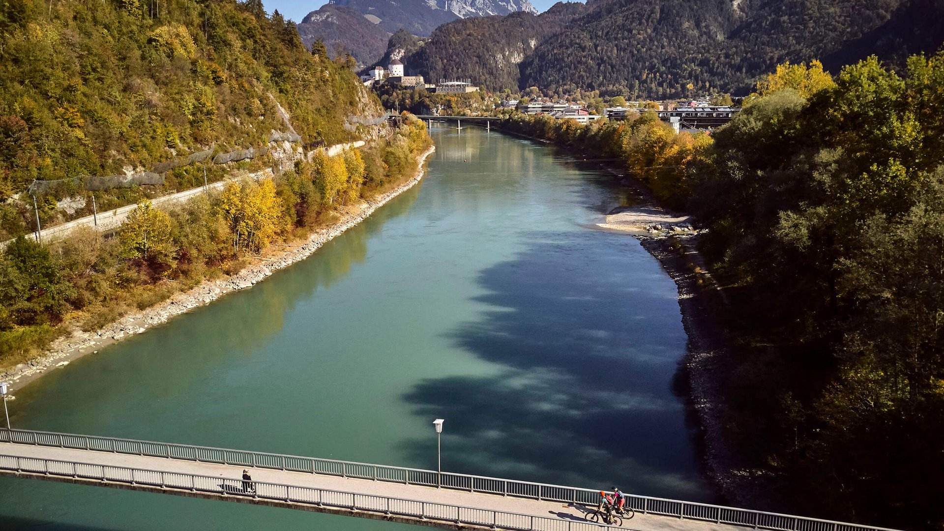 Bridge over a river with cyclists and mountains in the background