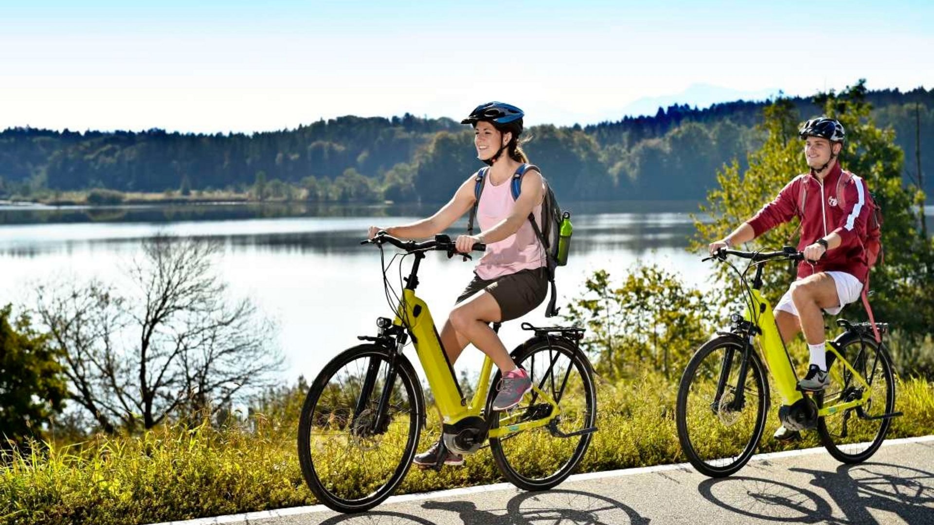 Two cyclists riding by a lake on a sunny day