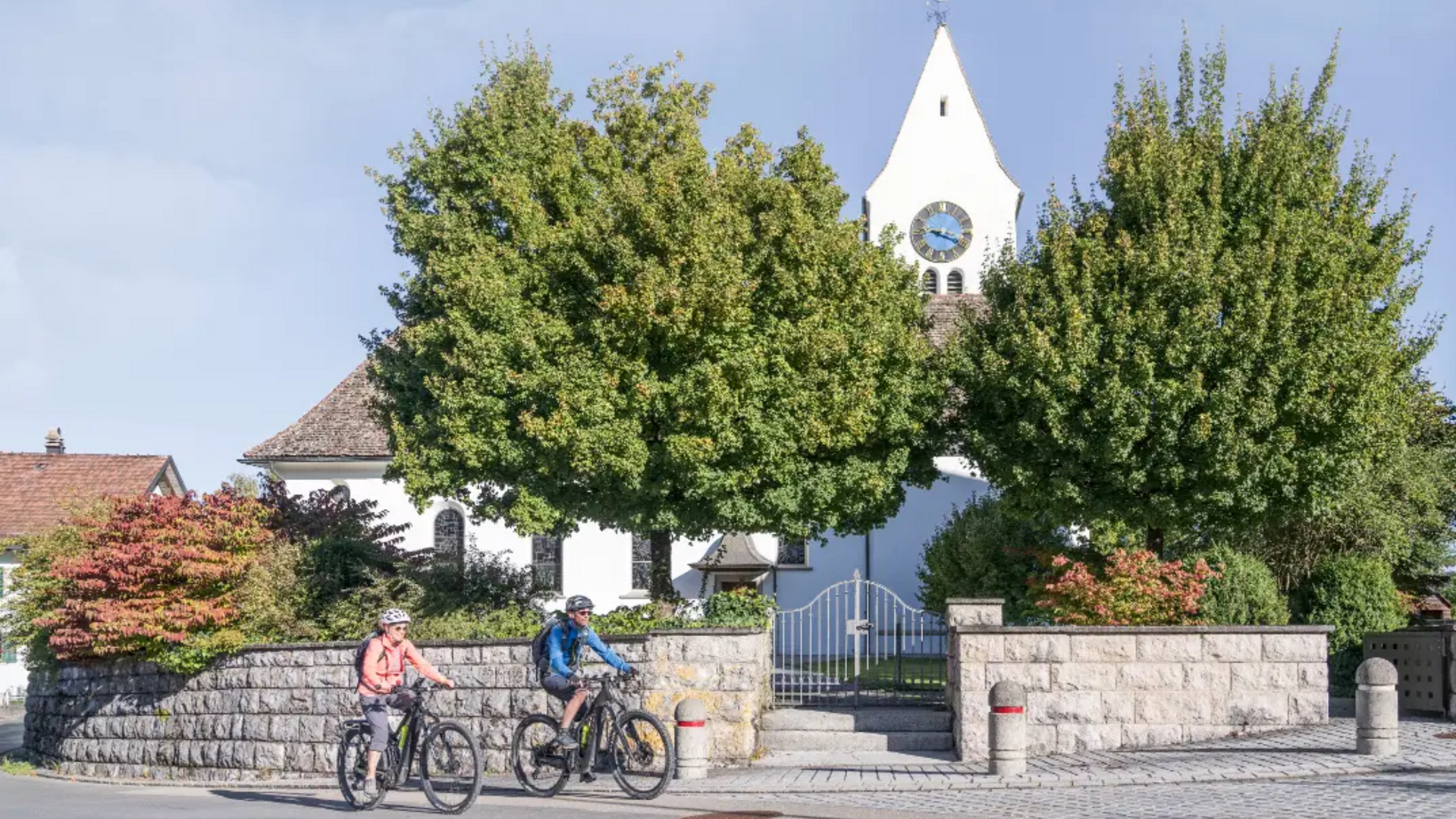 Two cyclists in front of a white church tower with a clock