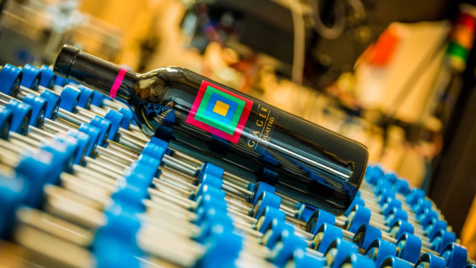 Fles Gager Quattro wijn liggend op blauwe transportband