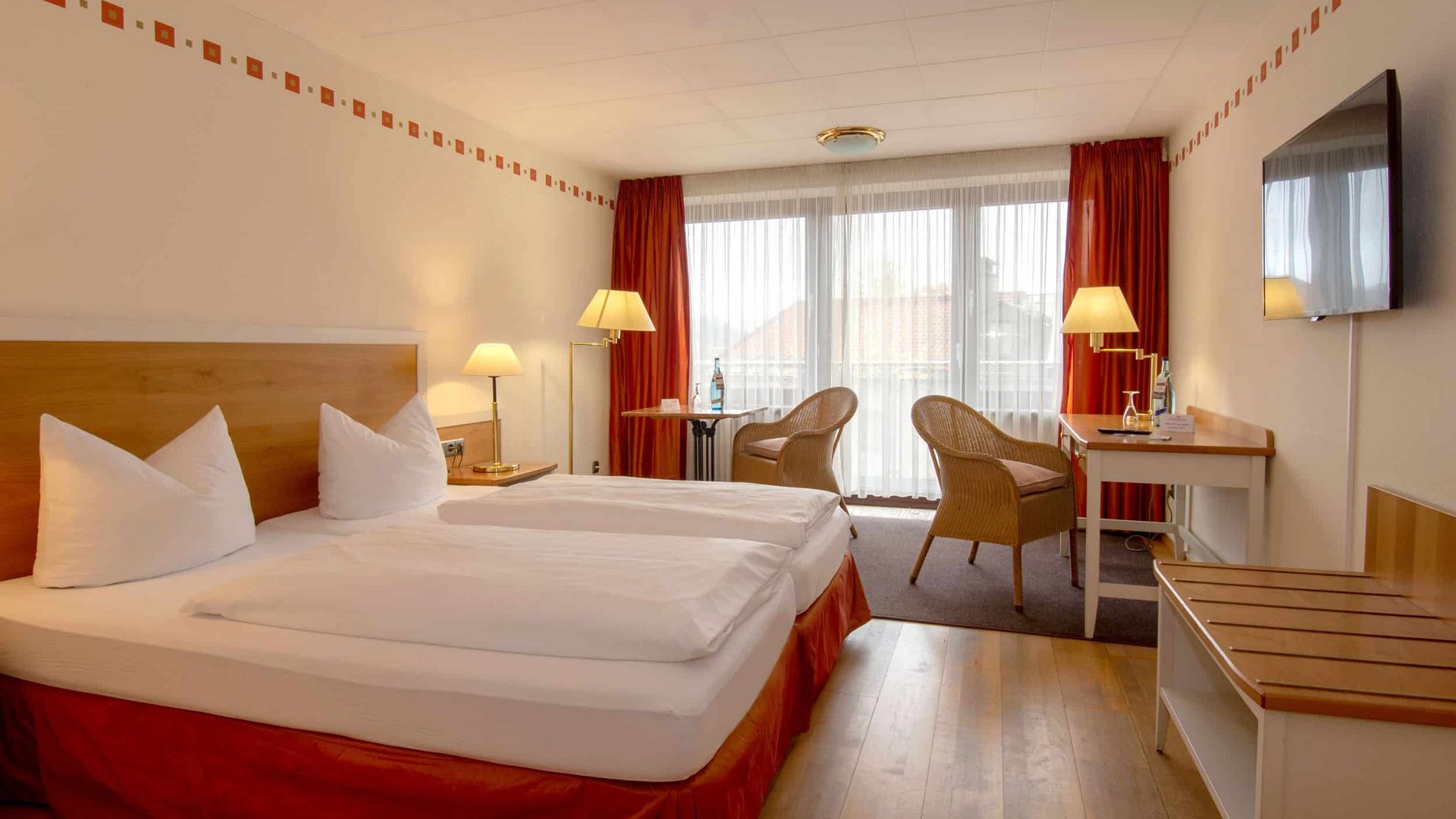 Bright hotel room with double bed, wooden floor, and two chairs