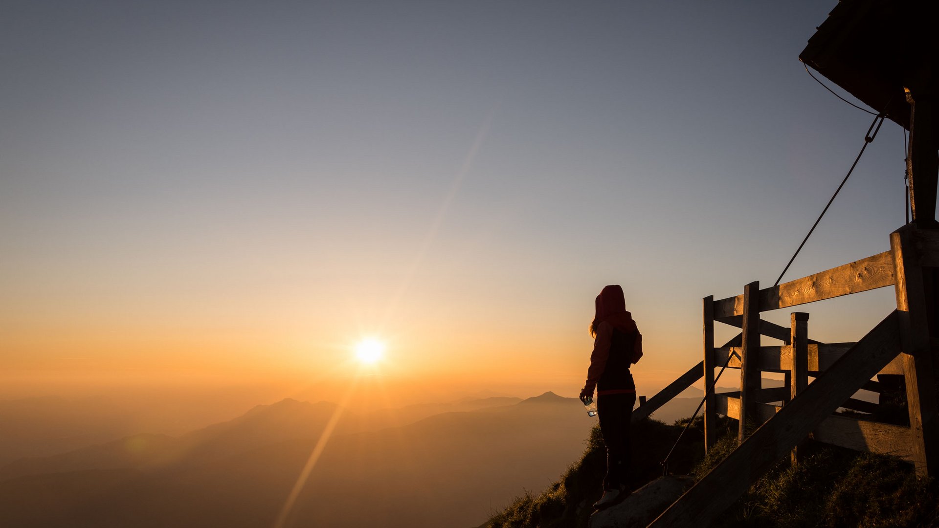 Person standing on mountain holding bottle watching sunset
