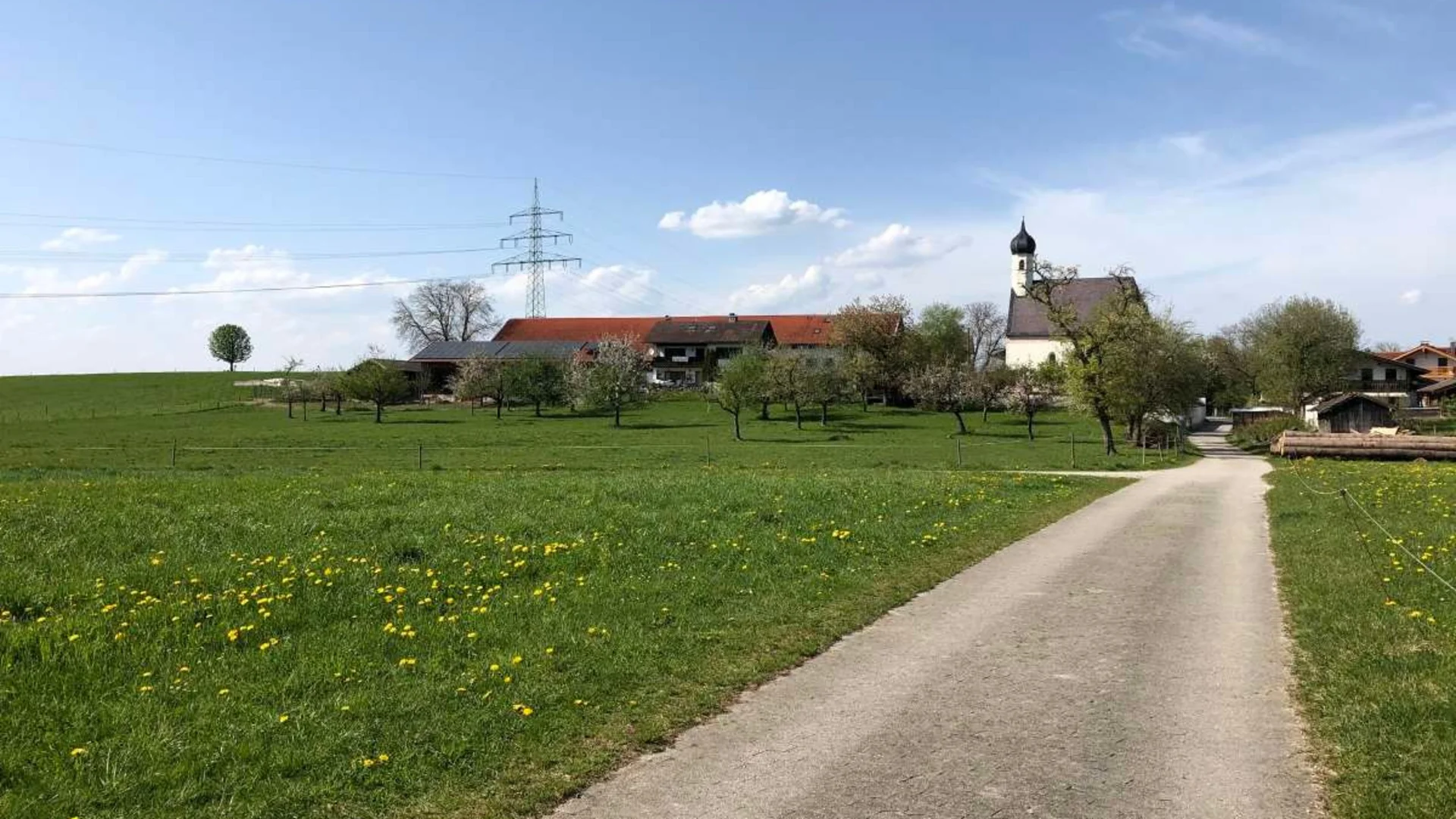 Landstraße führt zu Bauernhof und Kirche in grüner Frühlingslandschaft