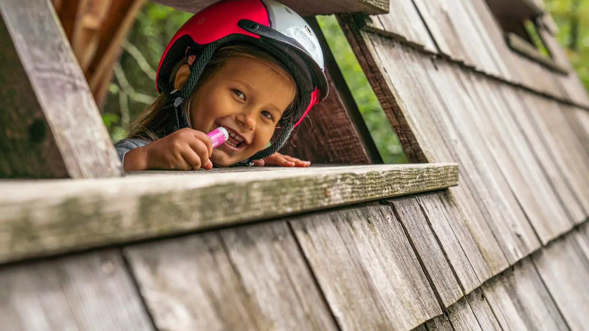 Kind met helm lacht en houdt lippenbalsem vast in houten speelhuis