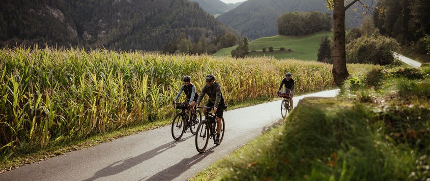Three cyclists ride on a country road through mountainous scenery