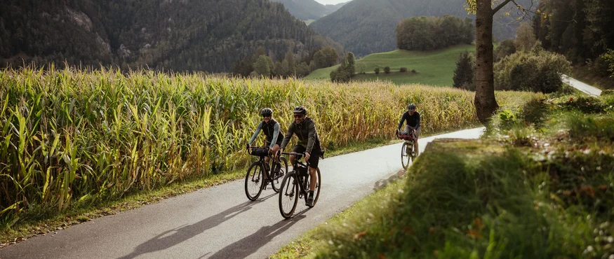 Drei Fahrradfahrer radeln auf einem Landweg durch eine bergige Landschaft