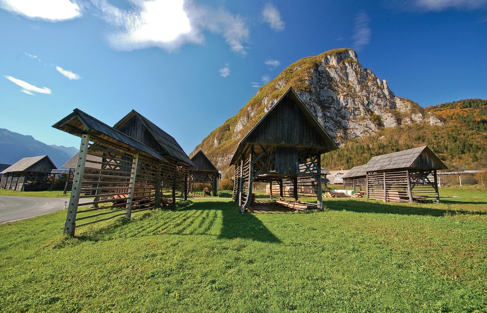 Slowenien © Turizem Bohinj - Alex Zdesar Traditionelle Holzhütten auf grüner Wiese vor Bergkulisse