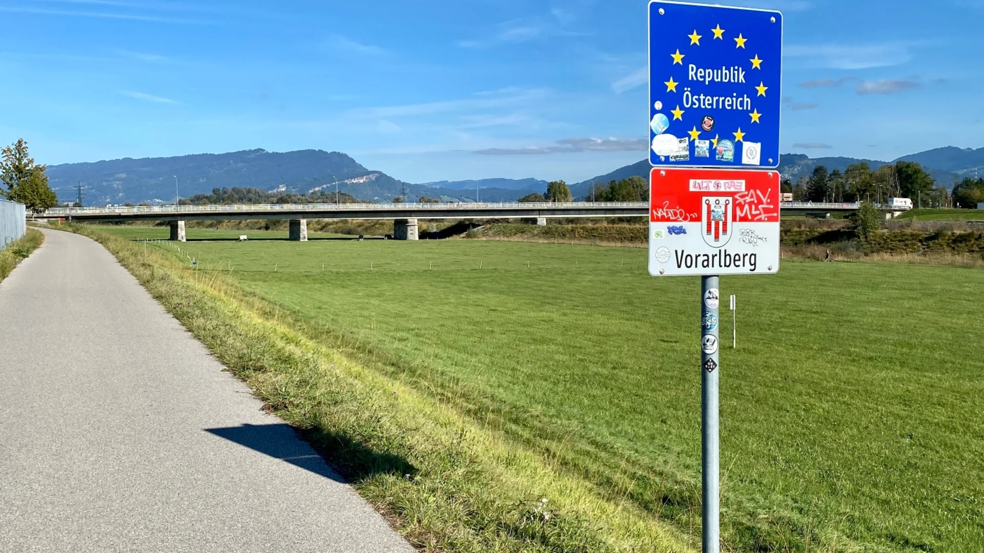 Grensbord Republiek Oostenrijk Vorarlberg naast fietspad bij zonnig weer
