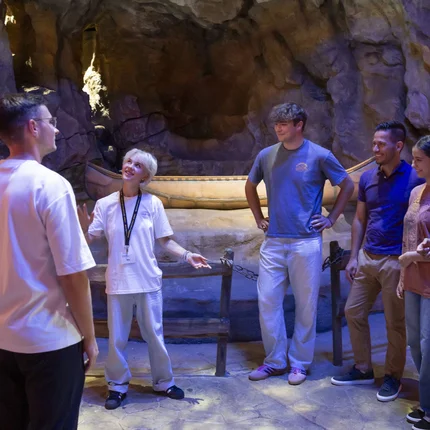 Filmreife Radelpause © Bavaria Filmstadt Eine Gruppe hört einem Guide in einer beleuchteten Höhle zu