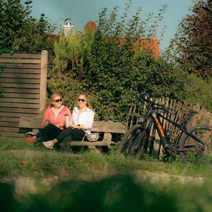 Two women sitting on a bench by bicycles in a natural setting