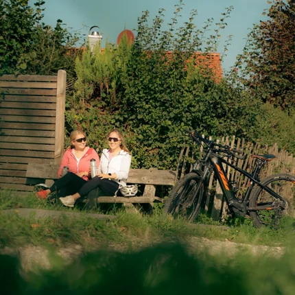 Twee vrouwen zitten op een bankje naast fietsen in de natuur