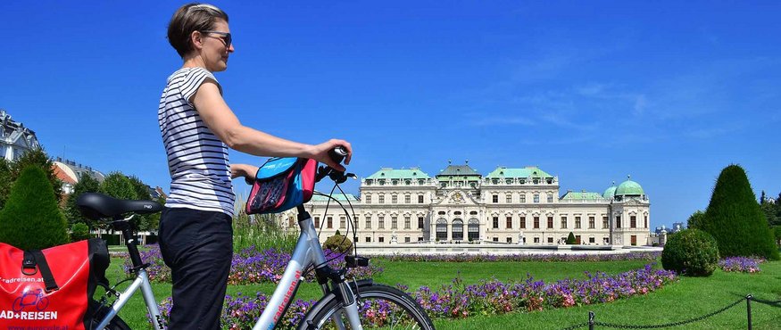 Woman with bicycle in front of Belvedere Palace and garden on a clear day
