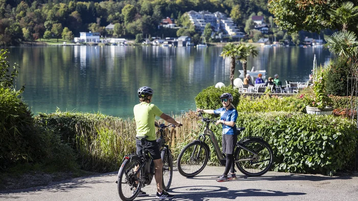 Klagenfurt kann mehr als Wörthersee! © Velontour - Heiko Mandl Zwei Radfahrer vor einem See mit Bergen und Bäumen im Hintergrund