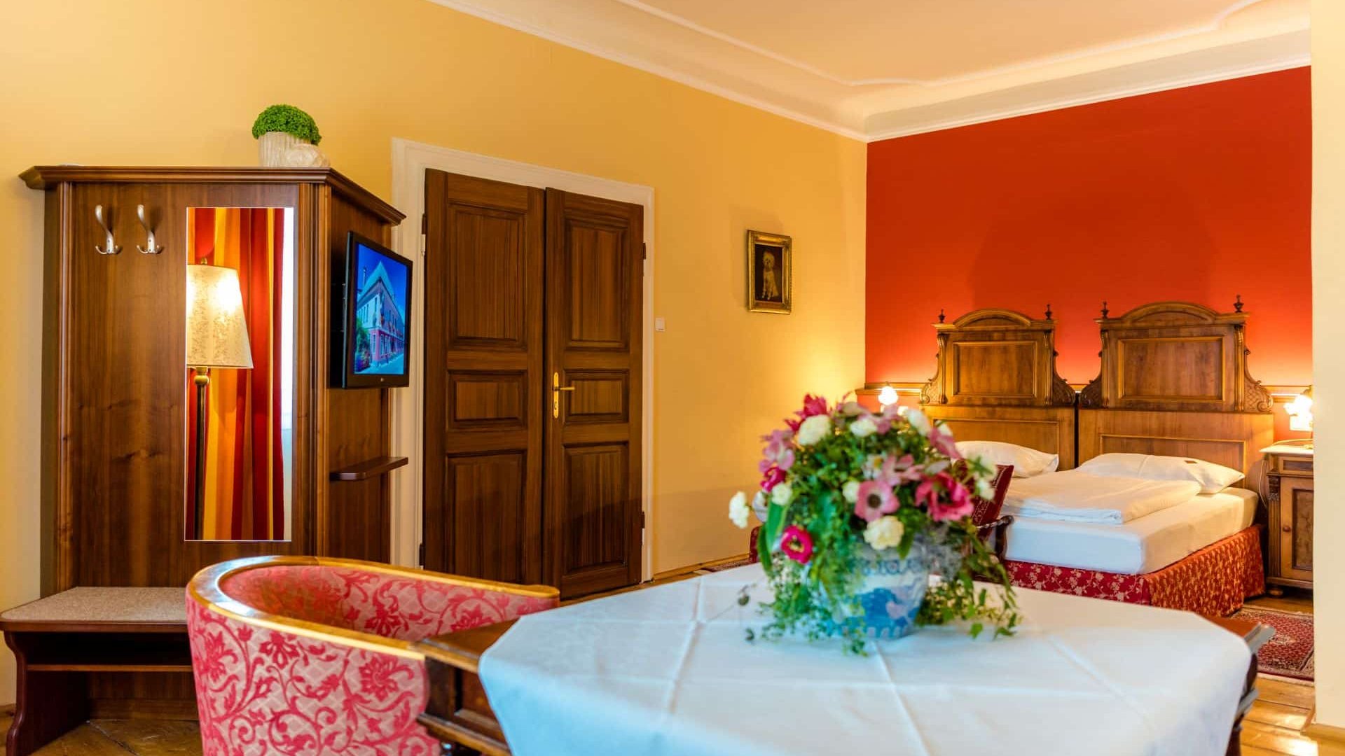 Bright hotel room with wooden furniture, bed, TV, and flowers on the table