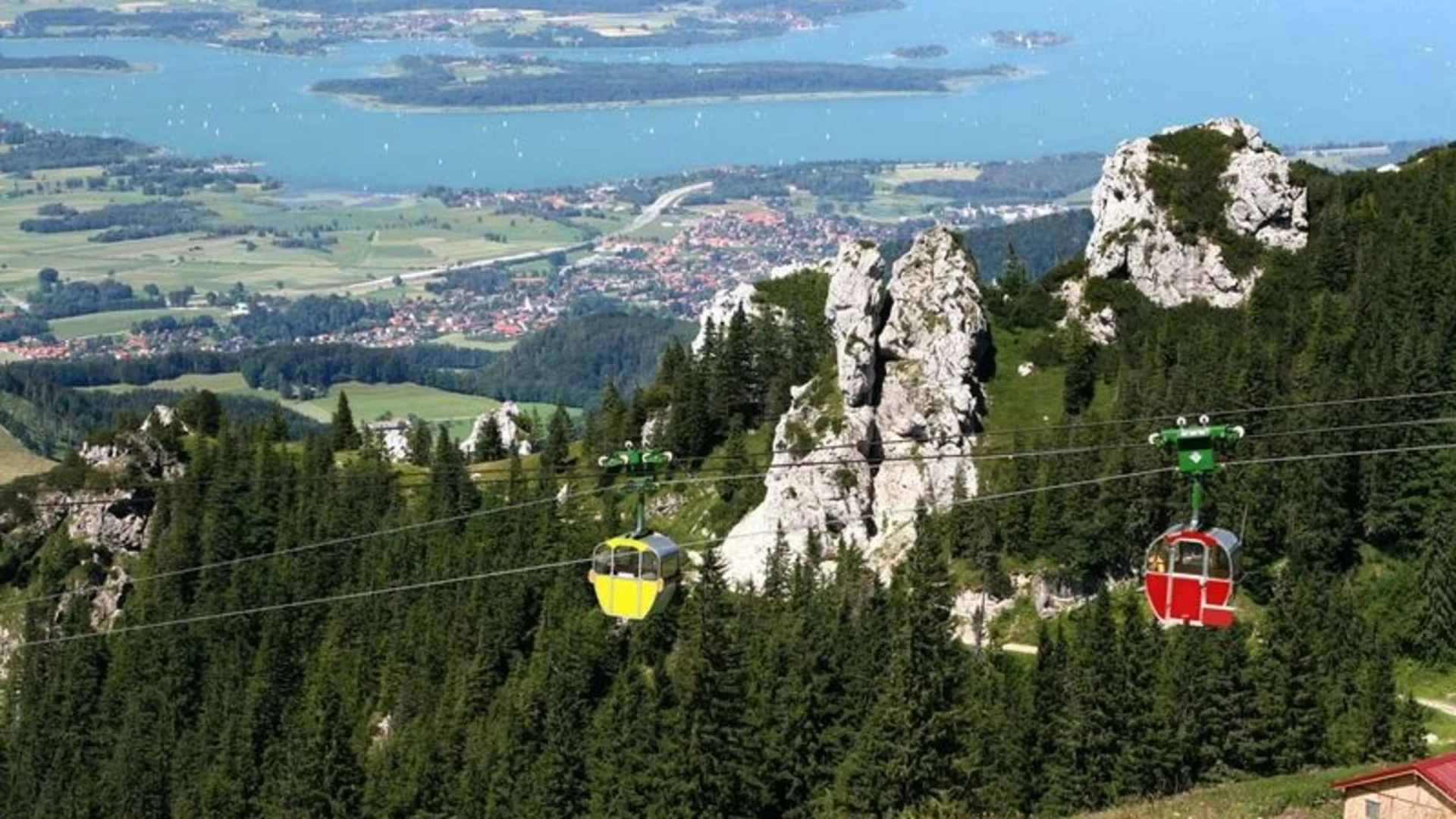 Seilbahngondeln über grünen Bergen mit Blick auf einen See und ein Tal