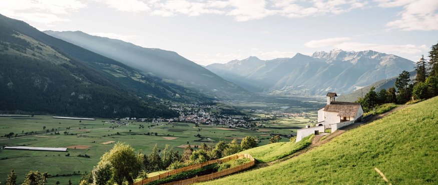 Mountain valley with church on green hill and sun rays through clouds