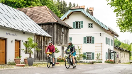 Zwei Radfahrer fahren vor einem historischen Museumscafé und Haus