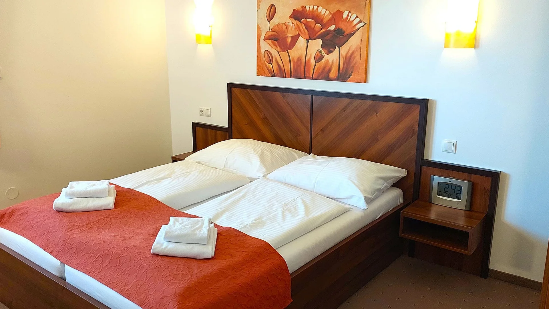 Gemütliches Hotelzimmer mit Doppelbett, roten Bettdecke und dekorativem Bild an der Wand