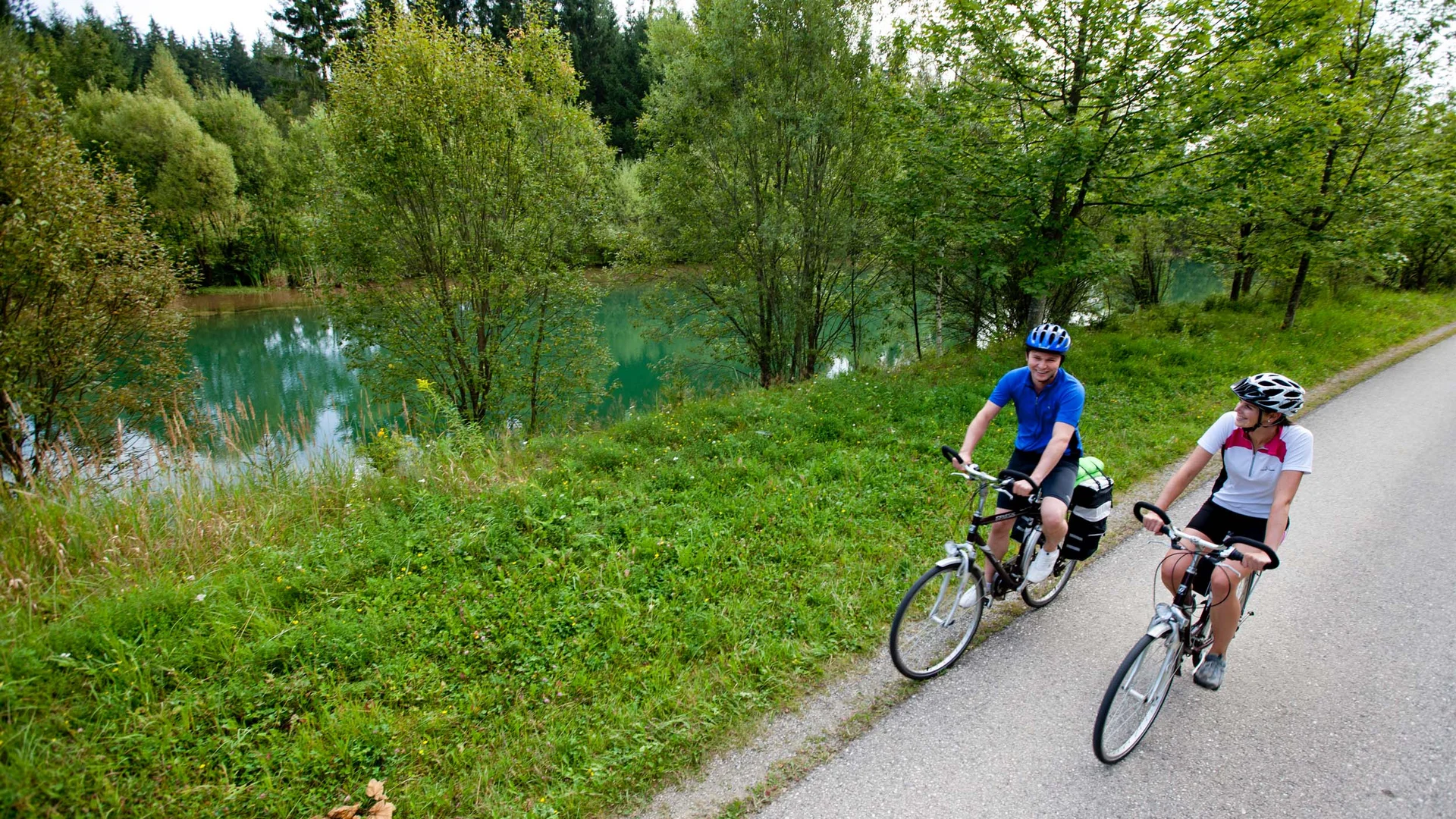 Twee fietsers op een pad naast een rivier en bomen