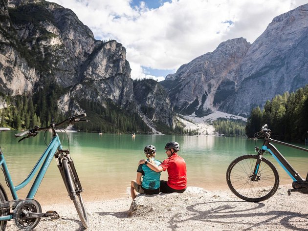 Paar mit Fahrrädern sitzt am See vor Bergen in sonniger Landschaft