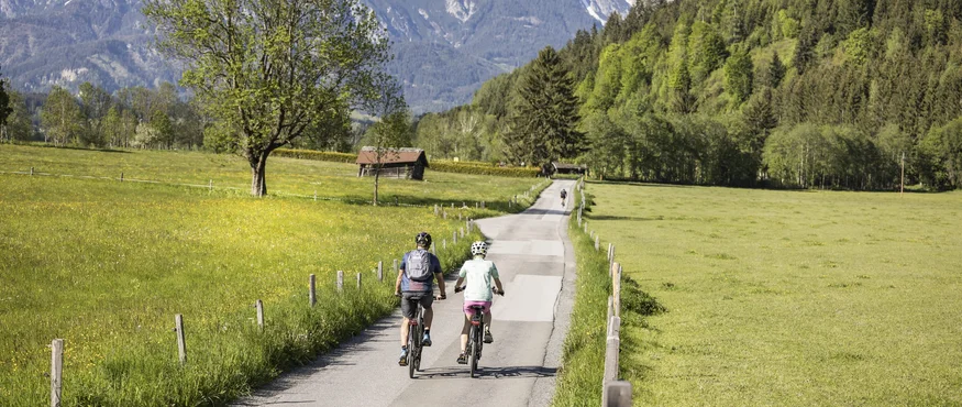5 Gründe, warum Maishofen der Geheimtipp für Genussradler ist © Velontour Zwei Radfahrer fahren auf einer Landstraße mit Bergen im Hintergrund