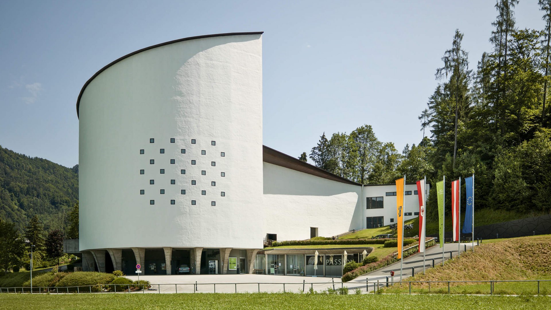 Modern white building with pillars by forest and colorful flags