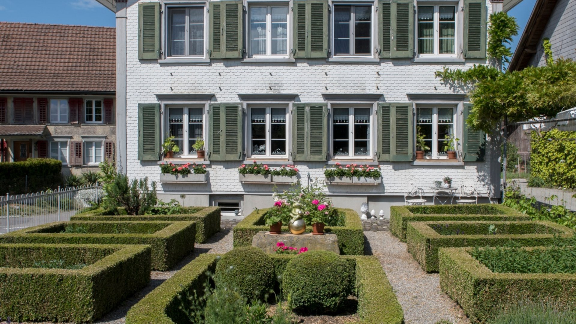 White house with green shutters and symmetrically trimmed garden