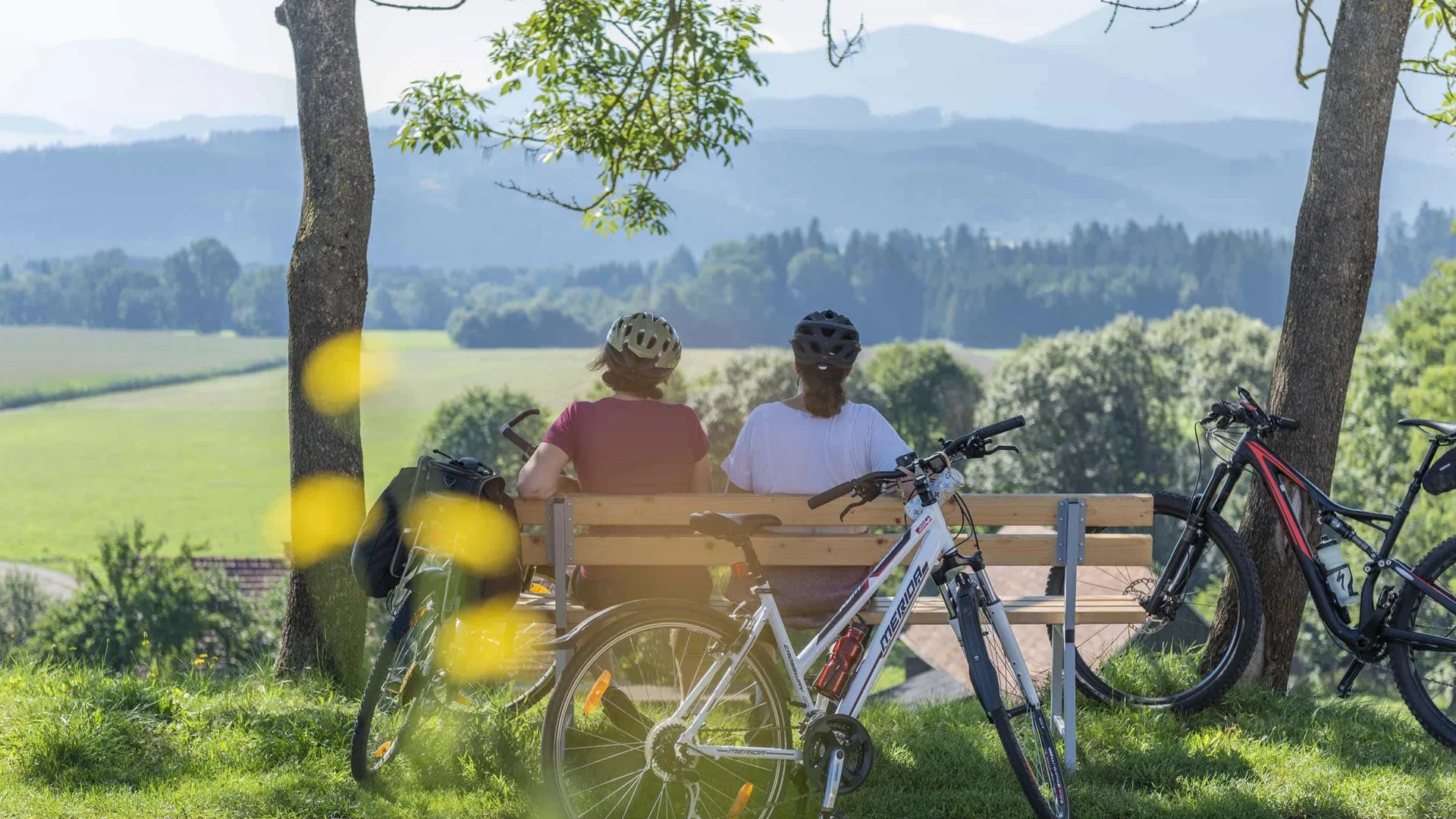 Twee fietsers zitten op een bankje met uitzicht op groene velden en bergen