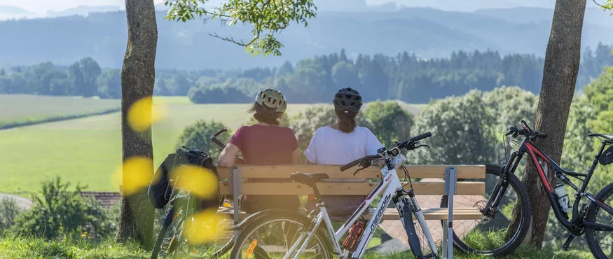 Twee fietsers zitten op een bankje met uitzicht op groene velden en bergen
