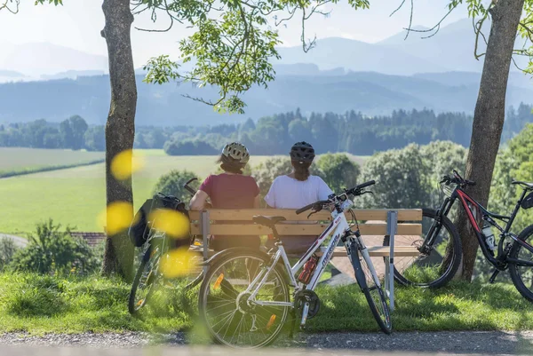 Von Genuss bis Rad im Murtal © Anita Fössl Zwei Radfahrer sitzen auf einer Bank mit Blick auf grüne Landschaft und Berge