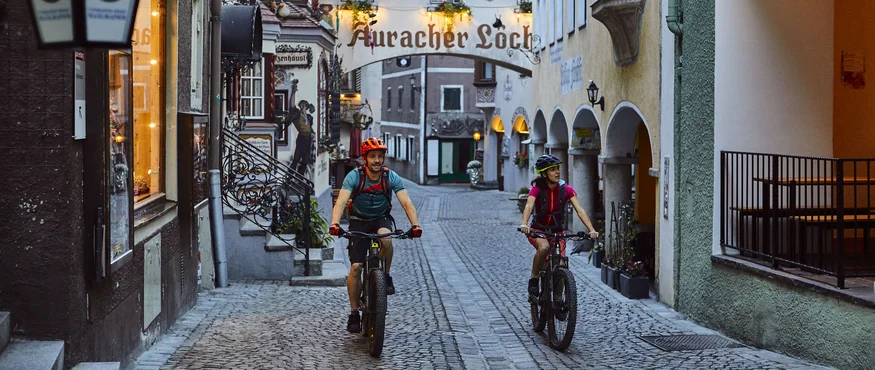 Zwei Radfahrer in einer engen, historischen Gasse mit Pflastersteinen