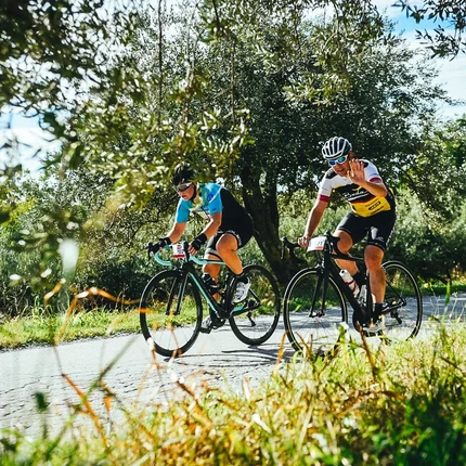 Twee wielrenners fietsen op een landweg omgeven door groen