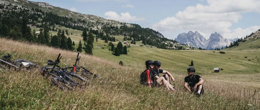 Personen machen Pause im Gras während einer Mountainbiketour in den Bergen