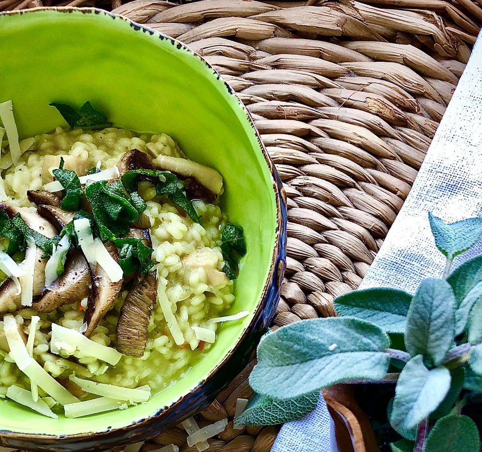 Green risotto with mushrooms, cheese, and fresh herbs in a green bowl