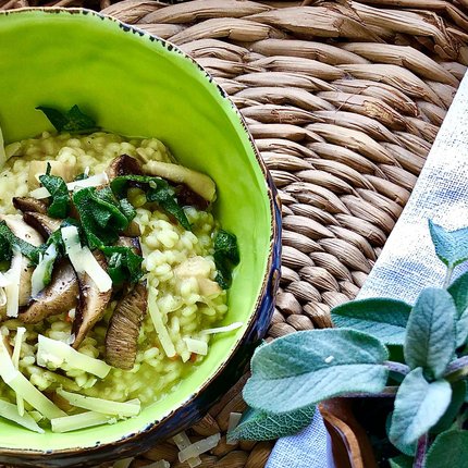 Green risotto with mushrooms, cheese, and fresh herbs in a green bowl