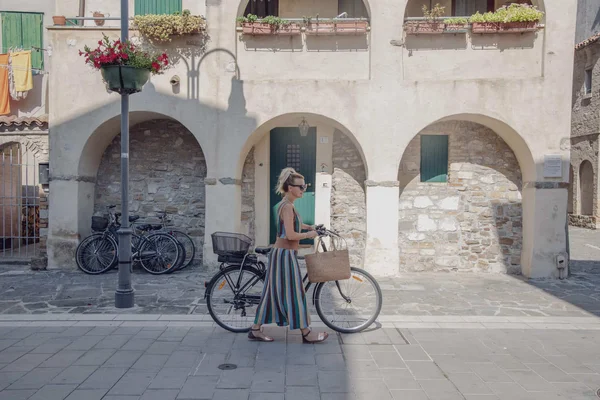 Grado: Herbst-Radeln an der Adria © Parentin Lara Frau schiebt Fahrrad auf gepflastertem Weg vor Gebäude mit Bögen
