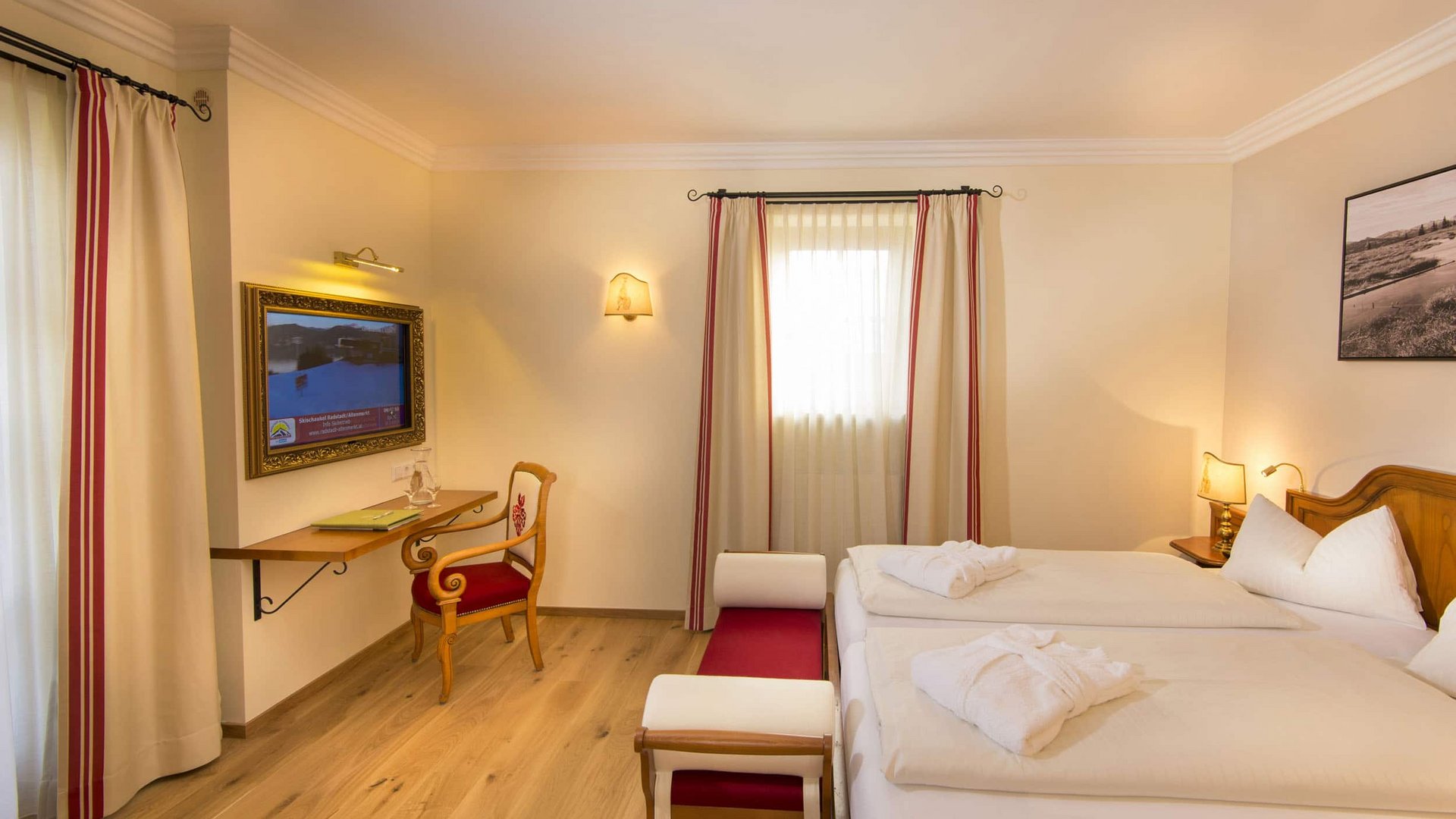 Bright hotel room with double bed, wooden floor and wall-mounted TV