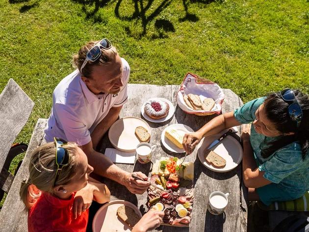 Drei Personen essen Picknick draußen neben Fahrrädern auf einer Wiese