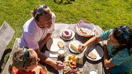 Drei Personen essen Picknick draußen neben Fahrrädern auf einer Wiese