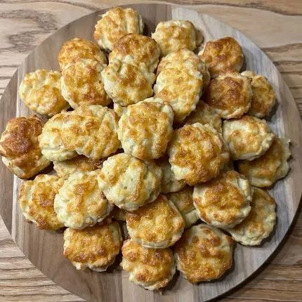 Platte mit kleinen überbackenen Käsegebäcken auf Holzuntergrund